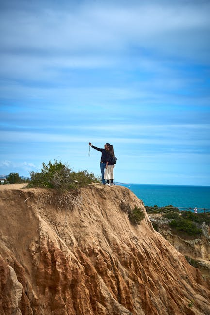 Two tourists take a selfie atop the Algarve cliffs in Distrito de Faro, Portugal, overlooking the ocean.